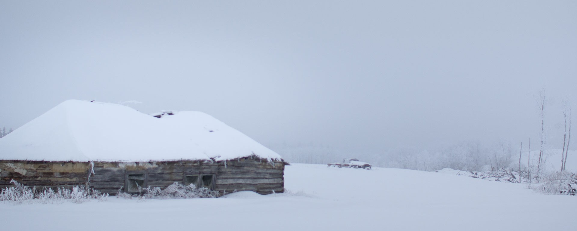 Abandoned log house in snowy field.