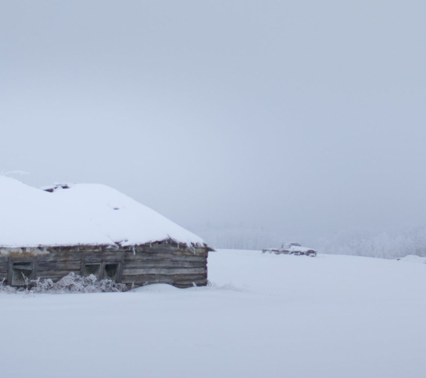 Abandoned log house in snowy field.