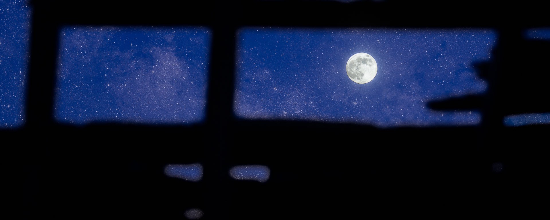 Starry night sky backdrops a full moon seen through a holey ceiling