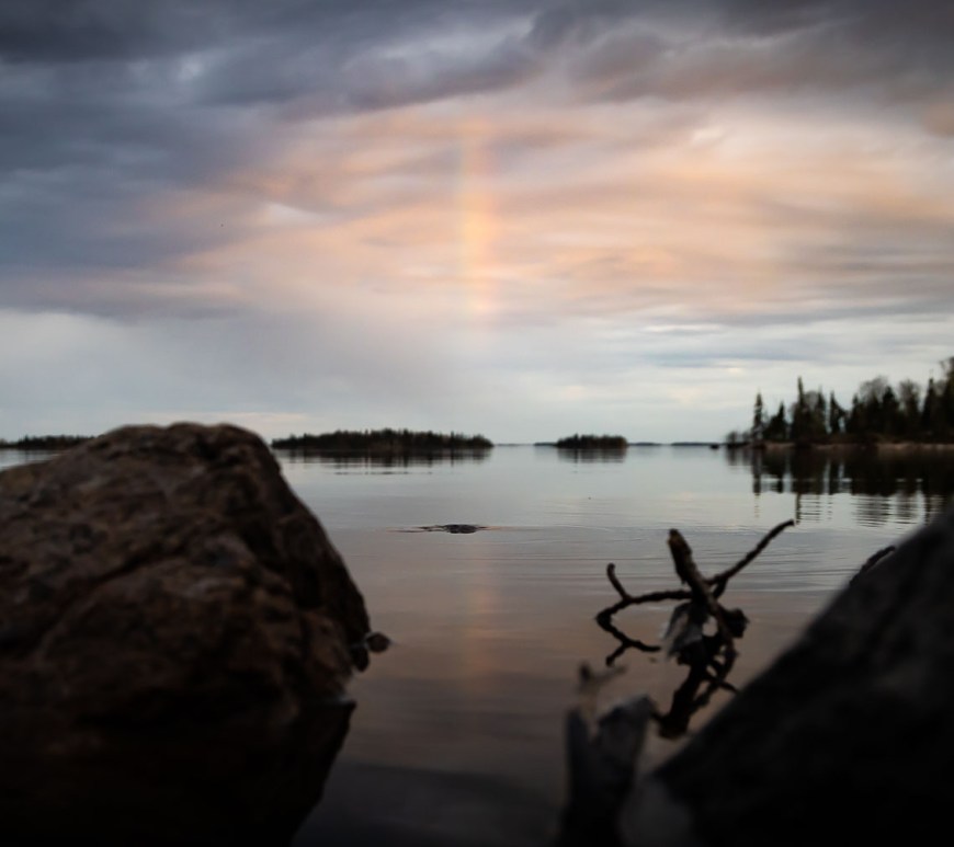 Dark clouds stretch out over a calm but Stoney lake a rainbow can be seen in the center.