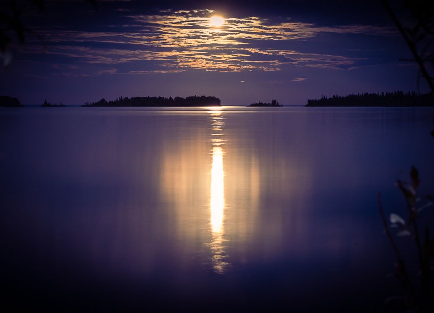 A golden full moon reflects across a clear blue lake.