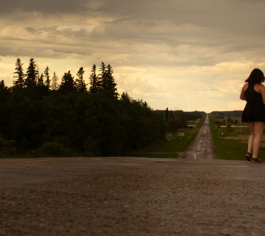 The sun sets on the open road as a woman looks on.