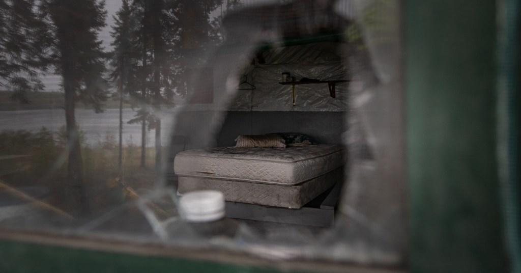 An abandoned bed seen through smashed glass.