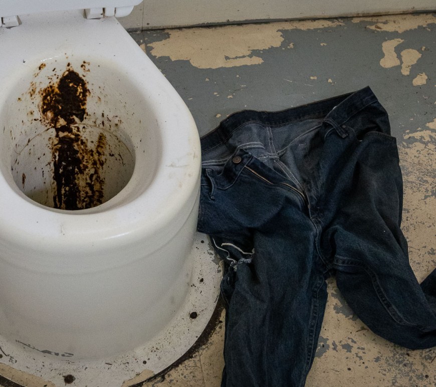 Feces sprayed on a toilet, next to an abandoned pair of jeans.