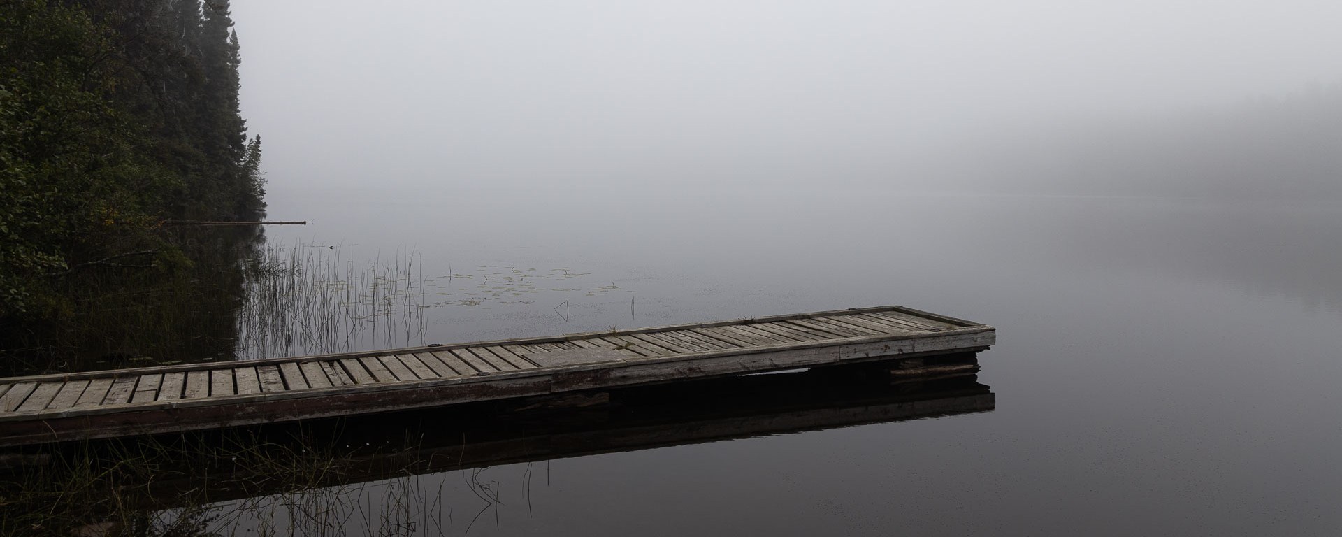 A rickety dock juts out on a smokey lake.