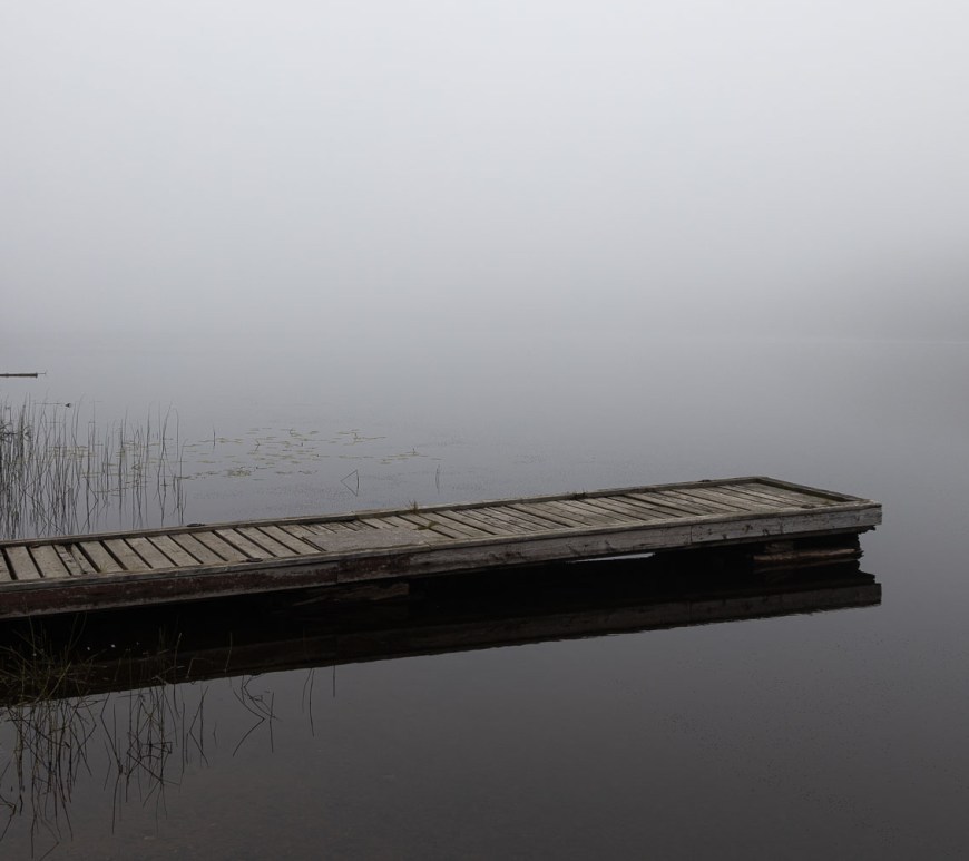A rickety dock juts out on a smokey lake.