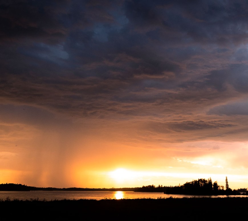 A storm falls over a lake at sunset.